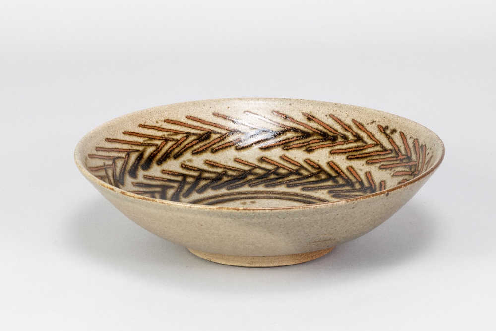 HELEN PINCOMBE (1908-2004); a shallow stoneware footed bowl with tenmoku breaking to kaki decoration