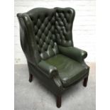 A George III style green leather wing back armchair with button back, on moulded front legs,