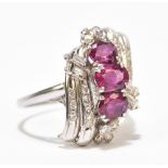 An 18ct white gold ruby and diamond ring, the three oval rubies above stepped platforms of