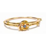 A sapphire and diamond set yellow metal bangle, formed as a knot with a central sapphire flanked