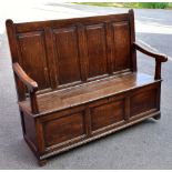 An 18th century oak settle, with four panel back and hinged seat, raised on block supports, width