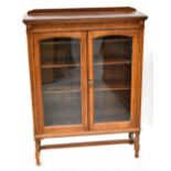 An early 20th century oak two-door display cabinet with simple frieze decoration above pair of