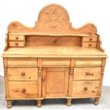 An early 20th century pine sideboard with arched back with carved decoration above a shelf flanked