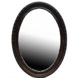 A dark stained carved oval wall mirror with inner and outer bands of carved decoration,