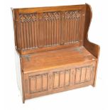 A modern oak Gothic-style wing back settle, with carved detail to the back and linenfold detail to