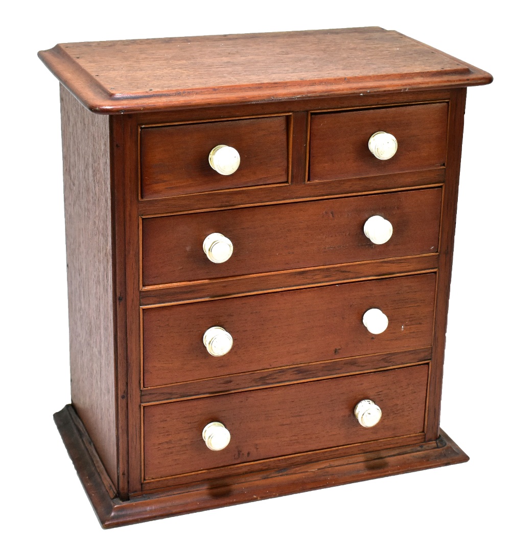 A late 19th century mahogany miniature chest of two short over three long drawers, with ceramics