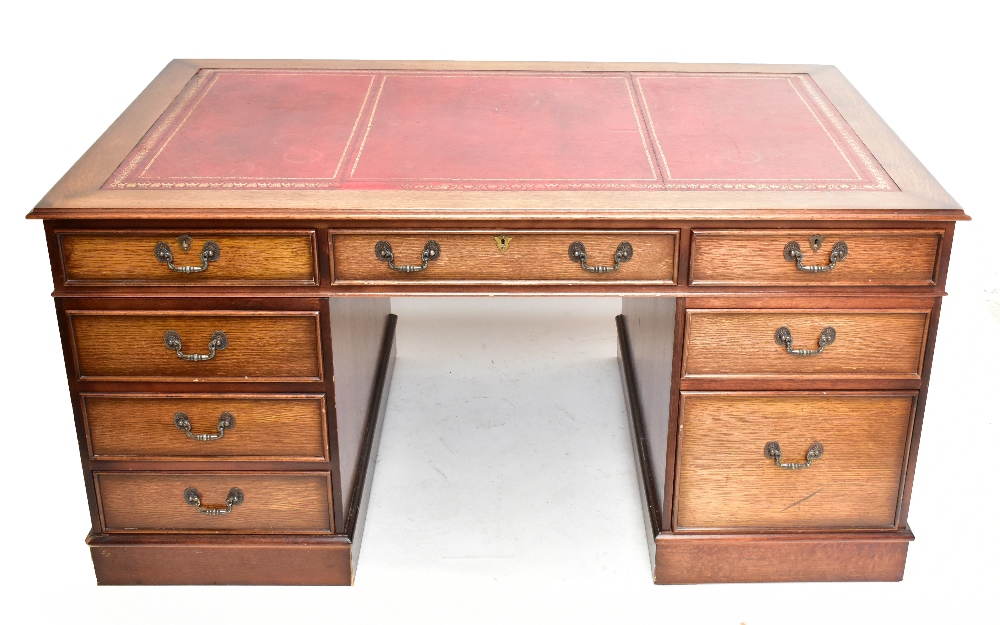 A reproduction oak veneered twin pedestal kneehole desk, with maroon leather inset top above an