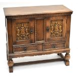 A reproduction oak cupboard with two carved doors above two drawers, raised on block feet, width