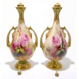 ROYAL WORCESTER; a pair of twin handled urn-form vases with gilt and hand painted rose blossom