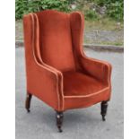 An Edwardian wing back armchair, upholstered in a deep red material, raised on turned column