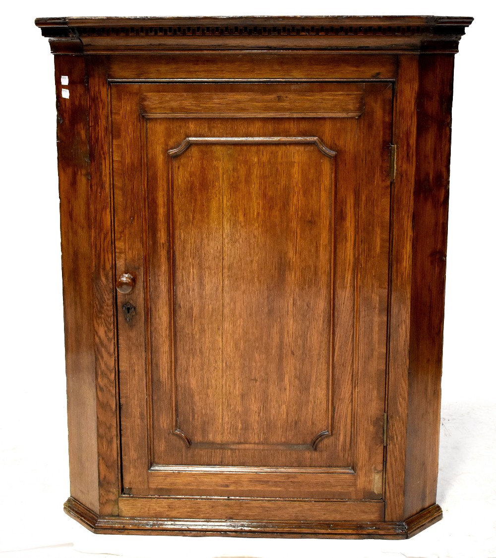 A George III oak wall hanging corner cupboard, three interior shaped shelves,