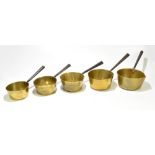 A graduated set of five brass saucepans, with copper riveted iron handles, the largest length