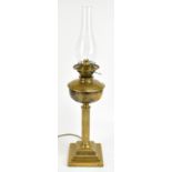 A brass oil lamp with clear chimney above fluted column to stepped square sectioned base,