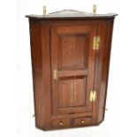 A George III oak hanging corner cabinet, with dentil cornice above a panelled door and two