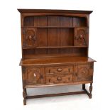 A 1920s Jacobean style carved oak high back dresser, the raised back with two panelled cupboard