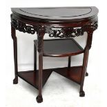 A 20th century Chinese rosewood demi-lune side table with carved skirt above three shelves, raised