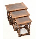 A reproduction oak nest of three graduated coffee tables, raised on turned column supports