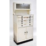 A vintage white painted dentist's cabinet, with glazed upper cupboard above six drawers and two