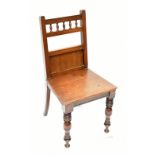 A Victorian oak hall chair with spindle stretcher, raised on turned column supports.