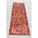 A hand knotted wool Heriz runner decorated with three medallions against a red ground with overall