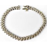 A silver tennis bracelet, the links in a chevron pattern, each set with three white stones,