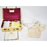 A selection of vintage linens, lace and other tableware, contained within a vintage cream suitcase.
