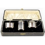 A George V hallmarked silver cased three-piece cruet set of oval form with domed lid,