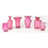 A small collection of cranberry glass comprising four jugs, a vase and a bottle,