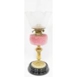 An Edwardian brass oil lamp with pink glass oil reserve to brass column and black stepped base,
