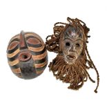 A Dan tribal mask with woven coiffure and adorned with shells and a Songe tribal mask with black,