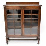 A 1920s oak two door display cabinet, with astragal glazed doors, on turned and block legs, height