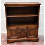 An oak open bookcase, with two shelves above two carved panelled cupboard doors, on bracket feet,