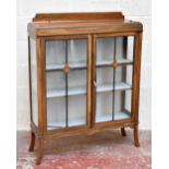 An early 20th century oak display cabinet, the two glazed doors enclosing two fixed shelves,