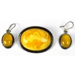A silver brooch set with oval honey amber and a pair of similar drop earrings (2).