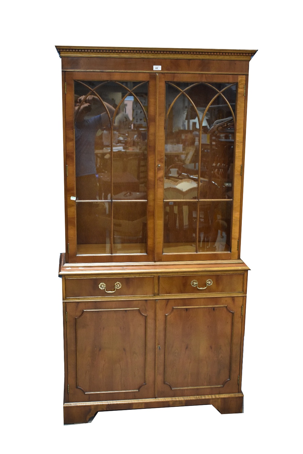 A reproduction yew wood bookcase with dentil moulded cornice above pair of glazed doors enclosing