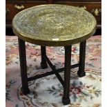 A brass Benares type circular table on a folding base with square section legs to spade feet.