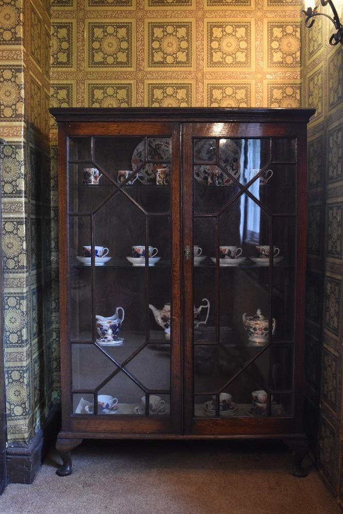 A 1920s oak display cabinet, with two astragal glazed doors enclosing glass shelves, on cabriole