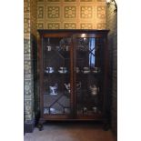 A 1920s oak display cabinet, with two astragal glazed doors enclosing glass shelves, on cabriole