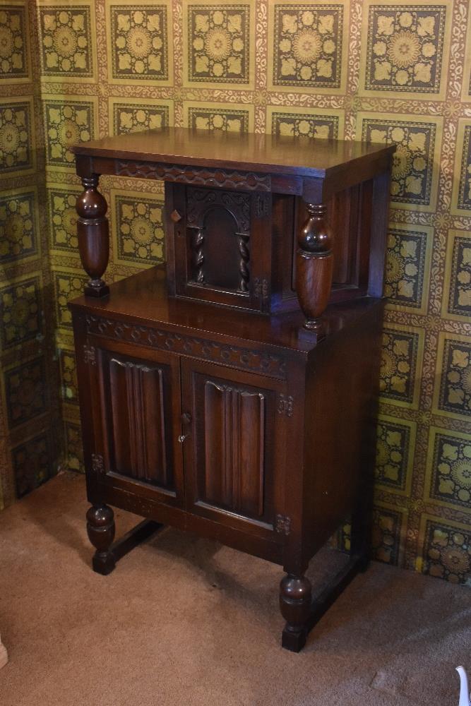 A 1940s carved and stained oak court cupboard, with arched panelled door above two linenfold