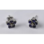 A pair of white metal floral set white and blue stone stud earrings.