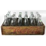 Twenty-two Coca-Cola bottles in clear and green glass within a Coca-Cola wooden sectional crate for