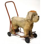 A mid-20th century toy push-along straw-filled dog, red painted frame, on black wheels,