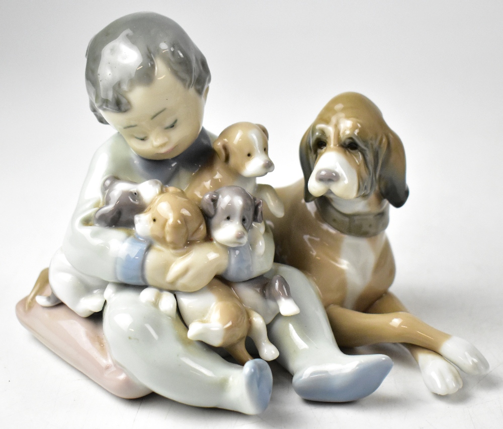 LLADRÓ; a young boy cuddling puppies with dog at his side.