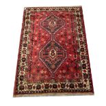 An early 20th century Middle Eastern red ground rug with repeating patterns and white floral border,