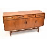 G PLAN; a 1970s teak sideboard with three drawers above four cupboard doors raised on shaped legs,