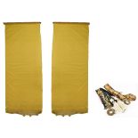 A pair of yellow cotton window blinds, with machine laced bottoms and brass cylindrical supports,