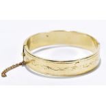 A yellow metal snap bangle with chased scrolling detail, stamped 14K, approximate weight 24.37g.