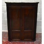 A George III mahogany hanging corner cabinet, with two panelled doors enclosing serpentine