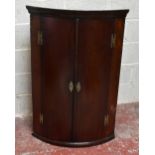 A George III inlaid mahogany bowfront hanging corner cabinet, with two doors enclosing white painted