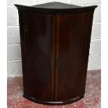 A George III mahogany bowfront corner cabinet, with two doors enclosing shelves and three drawers,